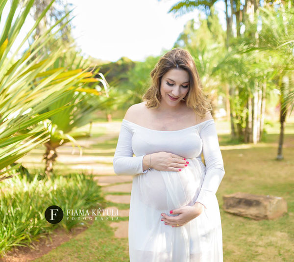 Grávida em ensaio fotográfico ao ar livre com vestido branco